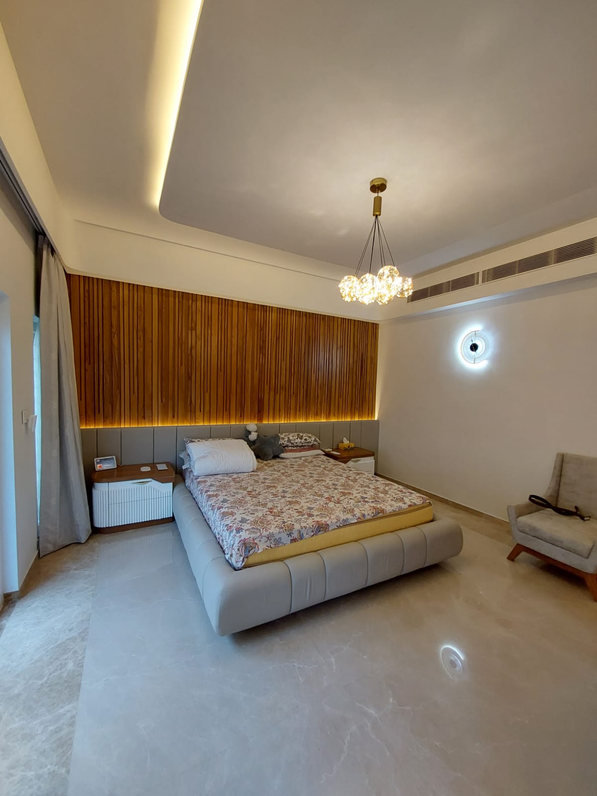 Grey bed with warm walnut slat wall & chandelier